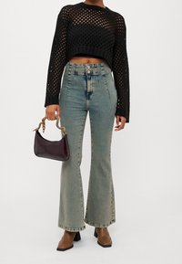 Maglione nero crop in rete con maniche lunghe, jeans azzurri svasati e borsa viola scuro con manico a catena dorata.