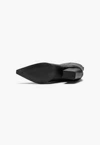 Zapato negro de tacón con puntera afilada y parte superior texturizada. Tacón cuadrado y suela de goma lisa con sutilezas para mejorar la tracción.