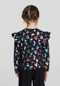 Czarna koszula z długim rękawem z wielokolorowymi nadrukami jednorożców i gwiazd. Falbany na ramionach dodają tekstury i detali do wzoru.