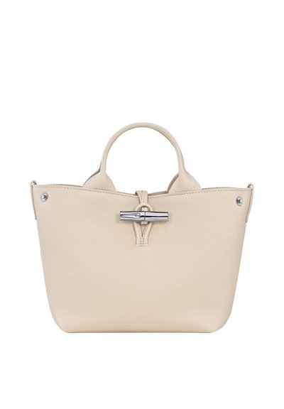 Beige leather handbag with a structured shape, top handles, silver hardware, and a distinctive closure detail. Textured surface with stitching accents.