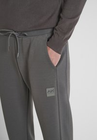 Grijze joggers met een zachte textuur, voorzien van zijzakken en een trekkoord in de taille. Inclusief een klein logo op de linker dij.