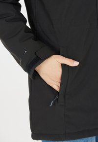 Sort vandtæt jakke med en lynlåslomme i siden og justerbare manchetter med velcro. Glat tekstur med en tætsiddende design.
