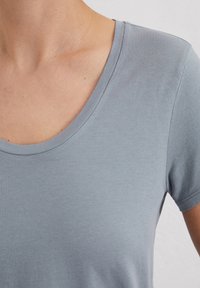 Jasnoniebieska koszulka z krótkim rękawem i okrągłym dekoltem. Wykonana z miękkiej tkaniny o gładkiej strukturze. Minimalistyczny design, bez widocznych wzorów.