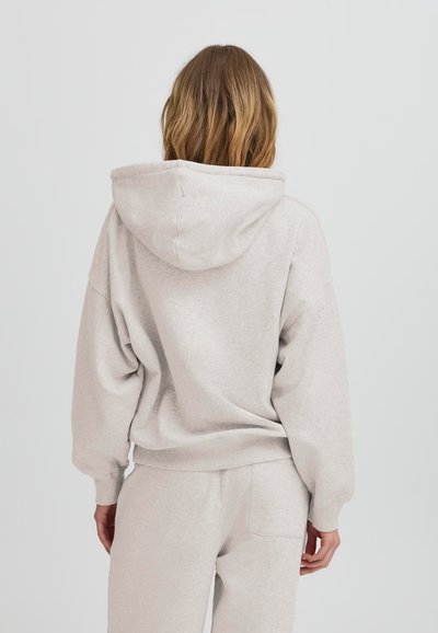 Svetlosivá mikina s veľkou kapucňou, spustenými ramenami a rebrovanými manžetami. Mäkkučký, štruktúrovaný materiál s voľným strihom, skombinovaný so zodpovedajúcimi teplákmi.