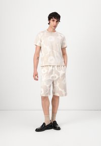 Lys beige matchende sett bestående av en kortermet skjorte og shorts med store, myke blomster mønstre. Bært med svarte loafers og kremfargede sokker.