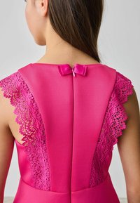 Fuchsia Kleid mit Spitzenakzenten auf den Schultern und einem Reißverschluss auf der Rückseite, verziert mit einer kleinen Schleife. Glattes, strukturiertes Material.