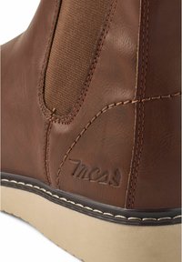 Bota de cuero marrón hasta el tobillo con paneles elásticos laterales, costuras en contraste y una suela de goma beige. Presenta un logo grabado en el costado.