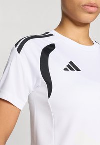 Λευκό αθλητικό πουκάμισο με μαύρες λεπτομέρειες στους ώμους και στο πλάι, κατασκευασμένο από διαπνέον υλικό με λεία υφή.