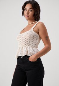 Nertinė palaidinė kreminės spalvos su peplum apdaila, su atvirais nėriniais. Sujungta su aukštu liemeniu juodomis džinsomis, pabrėžiančiomis figūrinę formą.