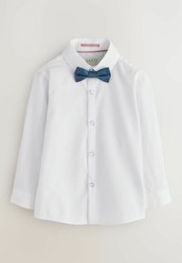 Camicia bianca a maniche lunghe con bottone frontale, caratterizzata da un papillon a motivi blu. Tessuto liscio con colletto classico e orlo arrotondato.