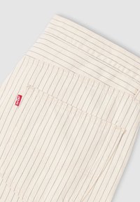 Μπεζ βαμβακερό ύφασμα με κάθετες μπλε ρίγες, διαθέτει πίσω τσέπη και κόκκινη ετικέτα Levi's. Ομαλή υφή και ραμμένο σχέδιο.