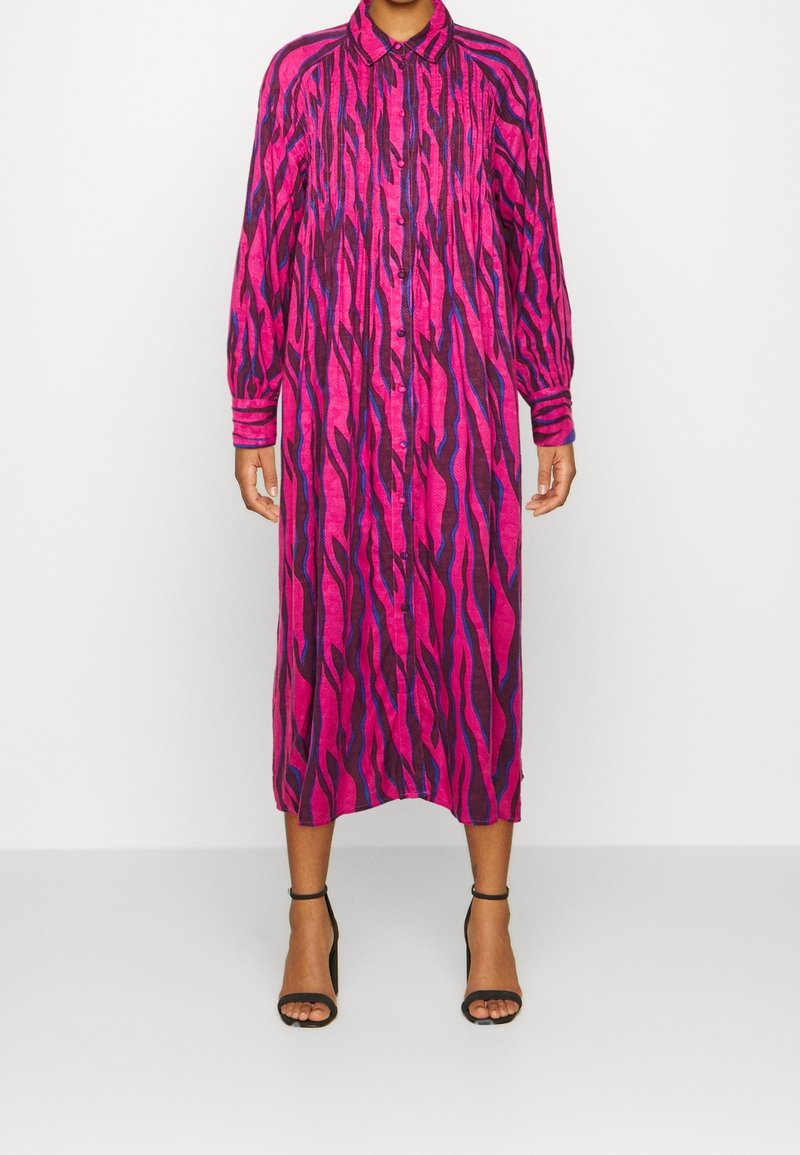 Robe midi à manches longues boutonnée avec des rayures abstraites ondulées roses, violettes et noires, portée avec des talons noirs à bride cheville.