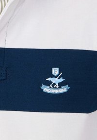 Tessuto a righe blu e bianco con un uccello azzurro ricamato che tiene una mazza da golf sopra un banner con la scritta "FACONNABLE"