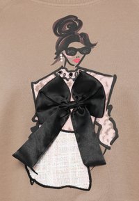 Brązowy sweter z ilustracją kobiety w kolorze czarnym i różowym, ozdobiony dużą czarną satynową kokardą w talii oraz perłowymi akcentami.