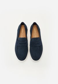 Chaussures à enfiler en suede bleu marine avec une semelle en caoutchouc blanc, dotées d'une sangle décorative et de coutures accentuées, conçues pour le confort.