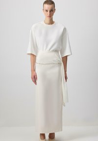 Top bianco over-size con maniche corte abbinato a una gonna lunga e aderente con cintura avvolgente e decorazioni dorate. Tessuto liscio.