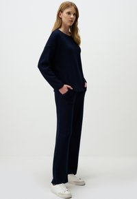 Navy blue knitted loungewear set with a textured pattern, featuring a relaxed-fit pullover and matching pants with side pockets. White sneakers.
