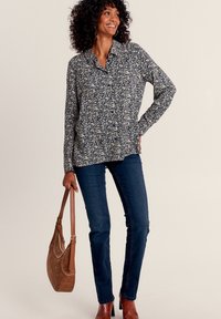 Hemd mit Blumendruck in Marineblau und Creme, kombiniert mit dunkelblauen Jeans und einer braunen Umhängetasche. Stiefel mit strukturierter Oberfläche.