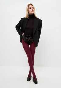Bordeaux pantyhoes gecombineerd met een zwart doorschijnend top, een zwarte jas en pailletten shorts, met glanzende zwarte schoenen met banddetails.