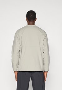 Veste matelassée gris clair avec une coupe décontractée, encolure ronde, poignets élastiques et une couture au dos, présentant une texture lisse.