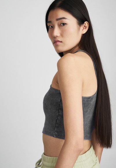 Šedý proužkovaný crop top s tenkými ramínky, s texturovaným povrchem a rovný výstřih, v kombinaci se světlými zelenými kalhotami na šňůrku.
