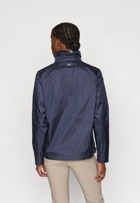 Granatowa kurtka wiatrówka z wysokim kołnierzem i lekko teksturowaną powierzchnią, z logo na plecach i długimi rękawami.