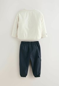 Steppjacke in hellem Creme mit rundem Ausschnitt, kombiniert mit marineblauen elastischen Hosen mit einer Cargotasche und elastischen Bündchen.