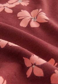 Maroon tyg med en mjuk textur, som har ljusrosa blommönster. Designen inkluderar överlappande blommor med detaljerade kronblad.