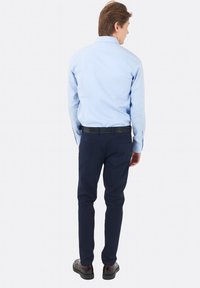 Camicia a maniche lunghe azzurro chiaro con colletto, abbinata a pantaloni slim-fit blu scuro e scarpe nere, vista da dietro.