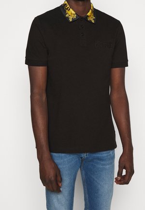 Polo noir avec un col à motif floral, manches courtes, et un détail de logo discret sur la poitrine. Confectionné en tissu de coton.