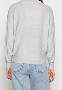 Pull en tricot gris clair avec une coupe décontractée, des poignets et un ourlet côtelés. Associé à un jean en denim bleu clair, mettant en valeur un style décontracté et confortable.