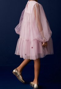 Rosa Tüllkleid mit Puffärmeln und gestufter Gestaltung, ausgestattet mit bestickten Blumendetails. Silberne Ballettflats runden den Look ab.