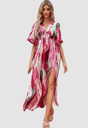 Mujer vestida con un vestido largo fluido de patrón rosa, blanco y verde, con mangas abullonadas y una abertura hasta el muslo, caminando hacia adelante sobre un fondo liso.