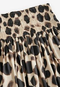 Jupe imprimée léopard avec des taches noires et brunes sur un fond beige. Dotée d'une taille smockée et d'un design plissé. Texture lisse.