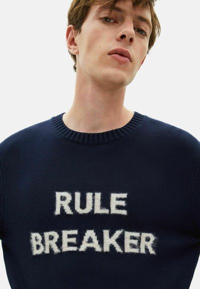 Maglione a maglia navy con colletto a coste, caratterizzato da testo bianco peloso "RULE BREAKER" sul petto. Vestibilità casual, tessuto testurizzato.