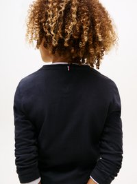 Navy long-sleeve shirt with rolled cuffs, rounded neckline, and a small logo accent on the back. Fabric appears smooth and soft.
