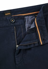 Marinblå byxor med dragkedja och knappstängning. Insidan har ett prickigt mönster och orangea detaljer längs midjebandet.