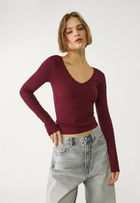 Haut à manches longues côtelé bordeaux avec un décolleté en V festonné, associé à un jean en denim gris clair taille haute au fit décontracté.