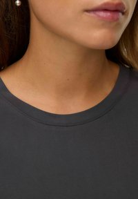 Mørkegrå T-shirt med rund hals. Glat stoftekstur med synlige sømme omkring kraven. Ingen udsmykninger bemærket.