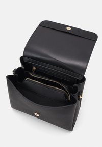 Sac à main en cuir noir avec une finition texturée. Il présente un rabat, des accessoires en doré et plusieurs compartiments intérieurs, y compris des poches zippées.
