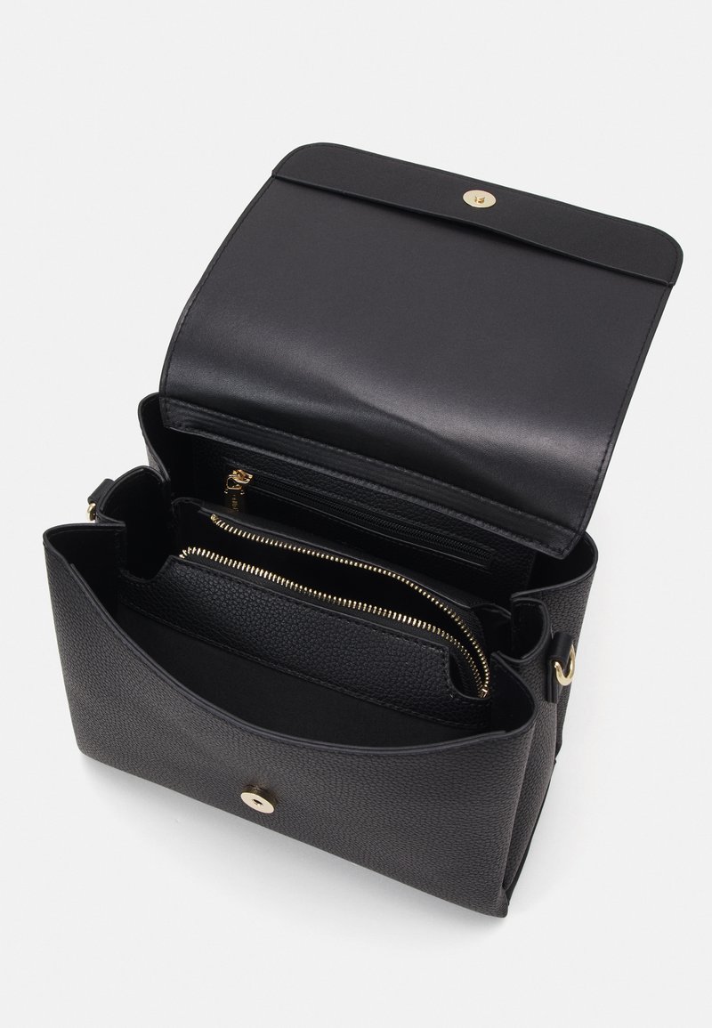Sac à main en cuir noir avec une finition texturée. Il présente un rabat, des accessoires en doré et plusieurs compartiments intérieurs, y compris des poches zippées.