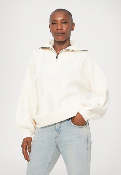 Suéter de punto color crema con cuello alto, media cremallera y patrones de diamante texturizados. Confeccionado en un material grueso, de corte relajado.