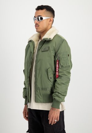 Giacca bomber verde con colletto in pelliccia sintetica, tasche con zip e un'etichetta di stoffa rossa. Texture liscia, chiusura con zip e polsini a costine.