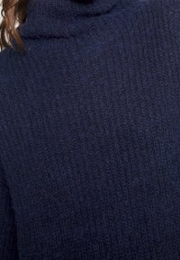 Mörkblå polotröja gjord av texturerat knittr material med ribbad detaljer och en mjuk yta.