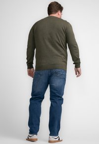 Olive green knitted sweater with long sleeves, round neckline, and ribbed cuffs. Paired with blue denim jeans and white sneakers.