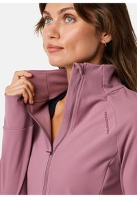 Fitted zip-up jacket in soft, lightweight pink fabric with a collar, featuring a logo on the shoulder and hidden zipper.