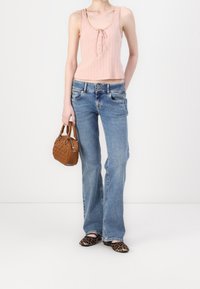 Top de tirantes de canalé rosa claro con un nudo en la parte delantera, combinado con jeans acampanados azules. Accesorios incluyen un bolso acolchado marrón y zapatos planos de estampado de leopardo.