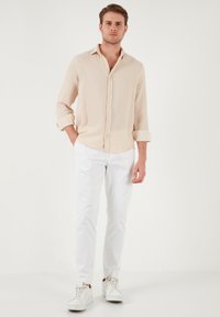 Camisa de rayas de color beige claro de manga larga con cierre de botones, combinada con pantalones ajustados blancos y zapatillas blancas. Diseño sencillo y casual.