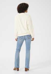 Maglione crema con maniche lunghe, abbinato a jeans svasati azzurri. Dettagli notevoli includono le cuciture sulle tasche posteriori e una vestibilità comoda.