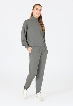 Grauer, langärmeliger Pullover mit halbem Reißverschluss, kombiniert mit passenden Jogginghosen; glatte Textur mit elastischem Bund und Taschen.
